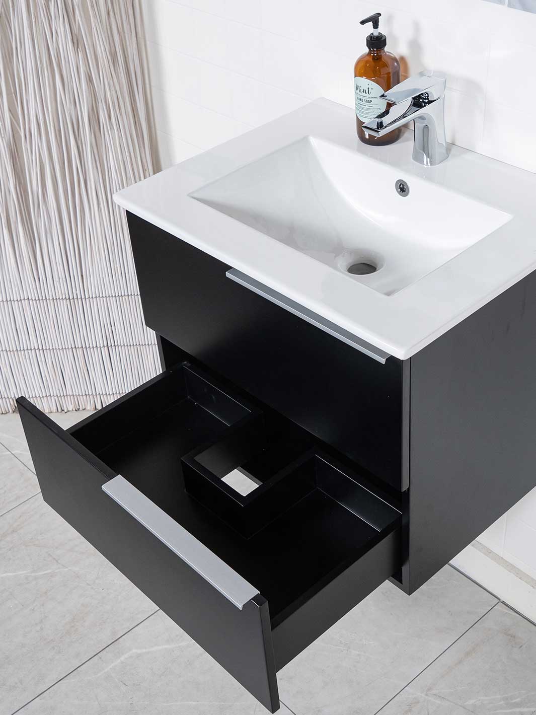 28 inch black floating vanity with bottom drawer open. White ceramic sink and chrome faucet.