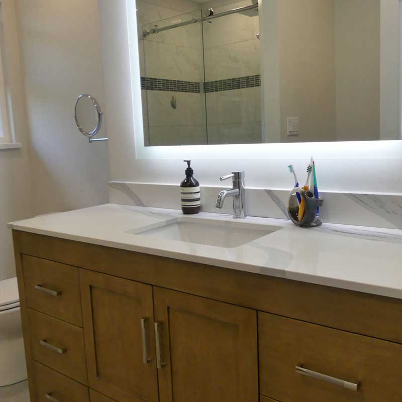 white oak bathroom vanity with sink, backlit mirror, and toiletries